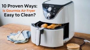 A Gourmia air fryer with cooked chicken and potatoes inside, placed on a wooden table with cleaning tools. The text overlay reads "10 Proven Ways: Is Gourmia Air Fryer Easy to Clean?" | Gourmia air fryer